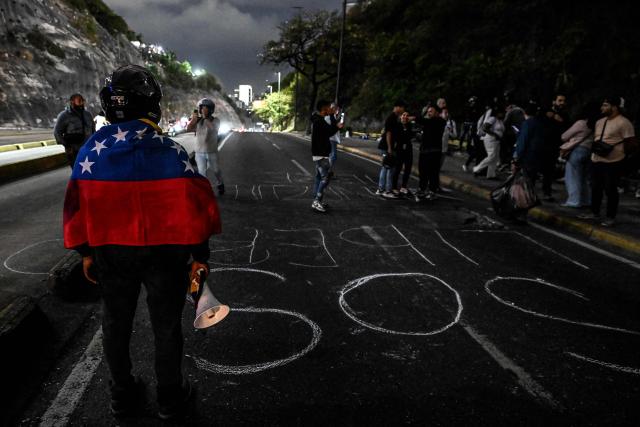 A demonstrator wrapped in a Venezuelan flag takes part in a demonstration to demand the freedom of political prisoners during a transfer outside El Helicoide prison in Caracas on June 3, 2026. (Photo by Juan BARRETO / AFP)