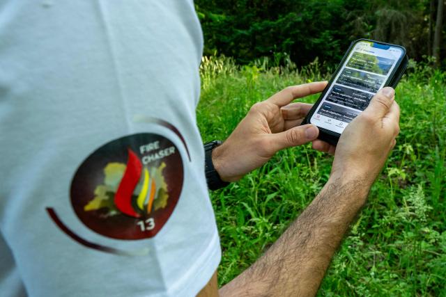 This photograph taken on May 21, 2026 in the Monteguait massif near Aix-en-Provence shows a member of the Fire Chaser association watching the Fire Chaser application on his cell phone. Founded in 2018 and recognised as being of public interest in 2025, Fire Chaser is a volunteer-run wildfire prevention association operating in the Bouches-du-Rhone department that developed a free mobile app allowing users to report and track fires in real time. (Photo by MIGUEL MEDINA / AFP)