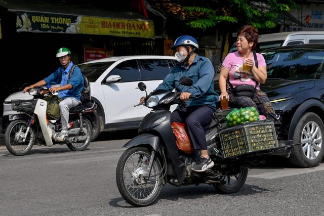 A woman holds drinks on the back of a motorbike in Hanoi on June 4, 2026. (Photo by Nhac NGUYEN / AFP)