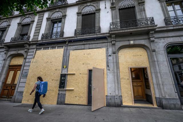 A passer-by walks past a building with its windows boarded up with wooden panels installed to protect the façade ahead of demonstrations against the G7 summit in nearby Evian, in Geneva, on June 4, 2026. Protests against the G7 summit in Evian are set to take place in nearby Geneva, where activists can gather more easily than in the tightly secured host town. (Photo by Fabrice COFFRINI / AFP)