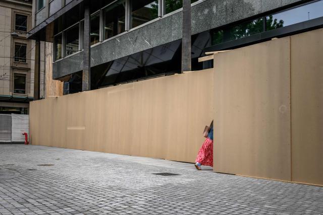 A woman enters an office building surrounded by wooden panels installed to protect the façade ahead of demonstrations against the Evian's G7 summit in Geneva, on June 4, 2026. Protests against the G7 summit in Evian are set to take place in nearby Geneva, where activists can gather more easily than in the tightly secured host town. (Photo by Fabrice COFFRINI / AFP)