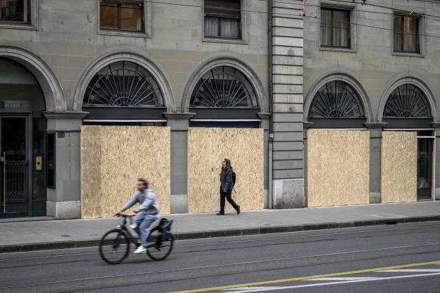 A passer-by walks past a building with its windows boarded up with wooden panels installed to protect the façade ahead of demonstrations against the G7 summit in nearby Evian, in Geneva, on June 4, 2026. Protests against the G7 summit in Evian are set to take place in nearby Geneva, where activists can gather more easily than in the tightly secured host town. (Photo by Fabrice COFFRINI / AFP)
