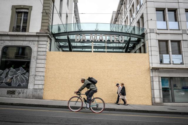 Passer-by walks past the entrance of a restaurant boarded up with wooden panels installed to protect the facade ahead of demonstrations against the G7 summit in nearby Evian, in Geneva, on June 4, 2026. Protests against the G7 summit in Evian are set to take place in nearby Geneva, where activists can gather more easily than in the tightly secured host town. (Photo by Fabrice COFFRINI / AFP)