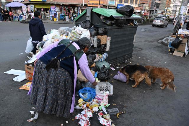 A woman rummages through accumulated garbage in the street in La Paz on June 4, 2026, amid growing political tensions and supply shortages affecting different regions of the country. The accumulation of waste in the city reached critical levels between late May and early June, posing a serious public health and environmental risk. The disruption of garbage collection services has been attributed to road blockades and, mainly, to a shortage of diesel fuel for collection trucks. (Photo by Aizar RALDES / AFP)
