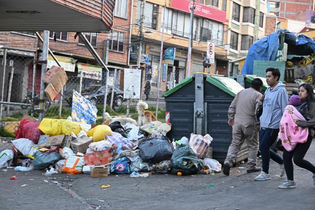 People walk past accumulated garbage in the street in La Paz on June 4, 2026, amid growing political tensions and supply shortages affecting different regions of the country. The accumulation of waste in the city reached critical levels between late May and early June, posing a serious public health and environmental risk. The disruption of garbage collection services has been attributed to road blockades and, mainly, to a shortage of diesel fuel for collection trucks. (Photo by Aizar RALDES / AFP)