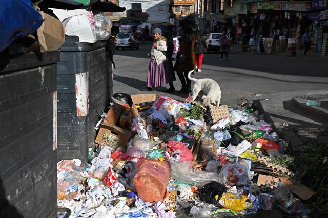 People walk past accumulated garbage in the street in La Paz on June 4, 2026, amid growing political tensions and supply shortages affecting different regions of the country. The accumulation of waste in the city reached critical levels between late May and early June, posing a serious public health and environmental risk. The disruption of garbage collection services has been attributed to road blockades and, mainly, to a shortage of diesel fuel for collection trucks. (Photo by Aizar RALDES / AFP)