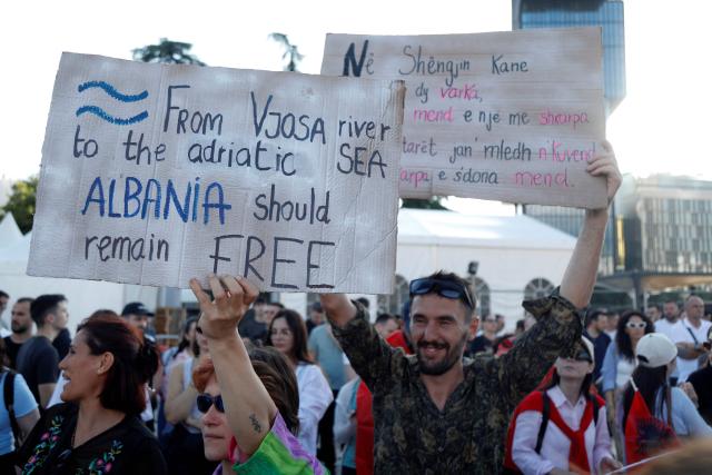 A demonstrator (L) holds a placard reading "From Vjosa River to the Adriatic Sea - Albania should remain free" as protestors gather in front of Albania's Prime Minister's Office during the 4th day of demonstration against the construction of a luxury resort near a protected natural area, in Tirana on June 4, 2026. Several thousand citizens demonstrated in Tirana for the second consecutive night to demand transparency around a tourist complex project allegedly linked to US President's son-in-law, Kushner. (Photo by AFP)