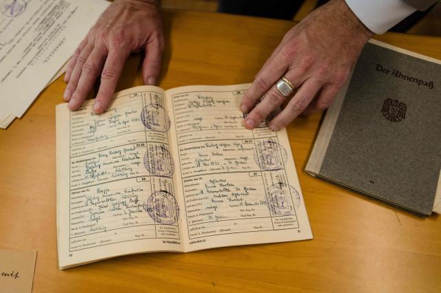 This photo taken on June 2, 2026 shows German lecturer Felix Puelm looking at the ‘ancestors pass’ book (C) of his grandfather Paul and the ‘ancestors pass’ book of Brigitte (R), at Silpakorn University, in Nakhon Pathom province, west of Bangkok. (Photo by ANTHONY WALLACE / AFP)