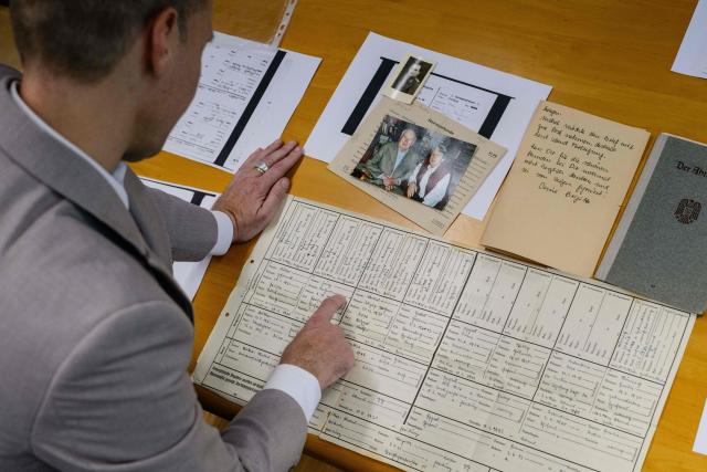 This photo taken on June 2, 2026 shows a picture of German lecturer Felix Puelm looking at the ‘ancestors pass’ documents of his grandfather Paul (C), printed copies of National Socialist German Workers’ party (NSDAP) membership passes of several family members, a picture of his grandparents Paul and Brigitte, a small picture of his grandfather, a personal letter written post war by Brigitte, and a printed copy of the NSDAP membership card of Brigitte (top C), that he found in an online database published by Die Zeit, a German national weekly newspaper, at Silpakorn University, in Nakhon Pathom province, west of Bangkok. (Photo by ANTHONY WALLACE / AFP)
