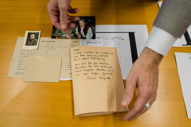 This photo taken on June 2, 2026 shows German lecturer Felix Puelm looking at (L-R) a war time picture of his grandfather Paul in army uniform, the marriage document of his grandparents Paul and Brigitte, picture of Paul and Brigitte as grandparents, a personal letter from Brigitte written post WWII, a printed National Socialist German Workers party (NSDAP) membership card of Brigitte that he found in an online database published by Die Zeit, a German national weekly newspaper, at Silpakorn University, in Nakhon Pathom province, west of Bangkok. (Photo by ANTHONY WALLACE / AFP)