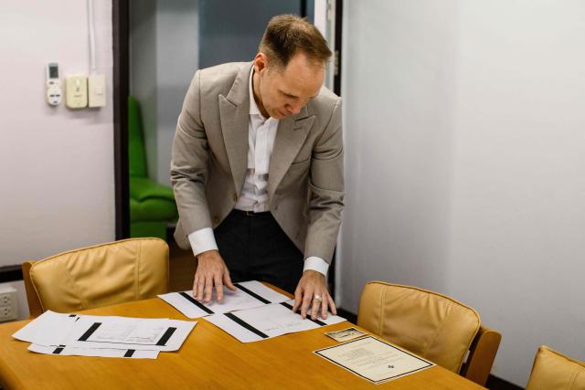 This photo taken on June 2, 2026 shows German lecturer Felix Puelm looking at printed copies of National Socialist German Workers party (NSDAP) membership cards of several members of his family (grandmother, great-grandfather, great-grandmother, several great-aunts, great-uncles), that he found in an online database published by Die Zeit, a German national weekly newspaper, and (R) a certificate of death of a great-uncle, at Silpakorn University, in Nakhon Pathom province, west of Bangkok. (Photo by ANTHONY WALLACE / AFP)