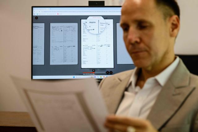 This photo taken on June 2, 2026 shows German lecturer Felix Puelm posing while holding a printed copy of the National Socialist German Workers’ party (NSDAP) membership card of his grandmother Brigitte, as shown on an online database (back C), published by Die Zeit, a German national weekly newspaper, at Silpakorn University, in Nakhon Pathom province, west of Bangkok. (Photo by ANTHONY WALLACE / AFP)