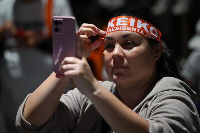 A supporter of Peru's presidential candidate for the Fuerza Popular party, Keiko Fujimori, use her mobile phone as she waits for her arrival at a closing campaign rally in Lima on June 4, 2026. Right-wing candidate Keiko Fujimori and leftist Roberto Sanchez will face off in Peru's presidential runoff on June 7, 2026. (Photo by MARTIN BERNETTI / AFP)
