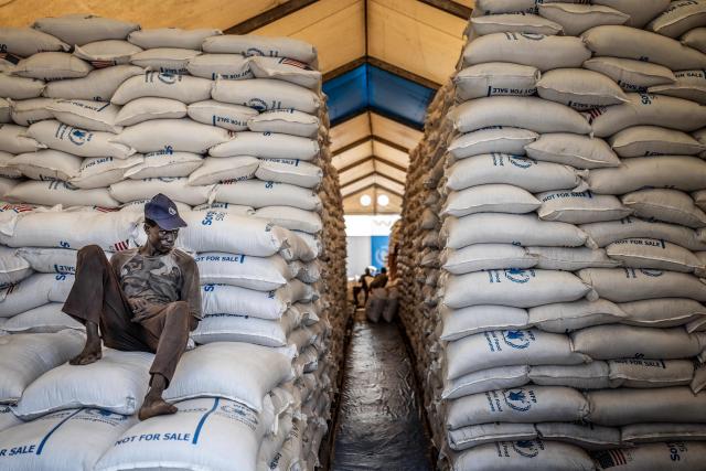 (FILES) A worker sits atop sacks of food aid in a hangar where supplies are piling up because deliveries are halted due to insecurity from the conflict, at a World Food Programme (WFP) warehouse in Bor, Jonglei State, on February 13, 2026. Hundreds of thousands displaced by conflict in South Sudan are increasingly forced to sell part of their rations to pay for basic needs at a time when the economy has almost entirely collapsed. One of the world's poorest countries, South Sudan has been mired in corruption and civil war for much of its existence since gaining independence in 2011. When US President Donald Trump ordered the shutdown of USAID last year, South Sudan lost a huge chunk of its humanitarian support at a time when nearly two-thirds of the population -- some 7.9 million people -- face acute hunger. (Photo by Luis TATO / AFP)