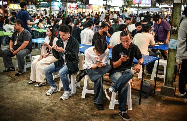 Customers check their phone as they wait to receive their order for lunch at a street-food market in Bangkok on June 4, 2026. (Photo by Amaury PAUL / AFP)