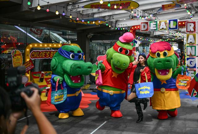 A model poses with crocodile mascots as part of a commercial photo session promoting sales outside a mall in Bangkok on June 4, 2026. (Photo by Amaury PAUL / AFP)