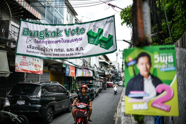A man rides his motorbike under a banner displayed ahead of the upcoming Bangkok gubernatorial election in Bangkok on June 4, 2026. (Photo by Amaury PAUL / AFP)