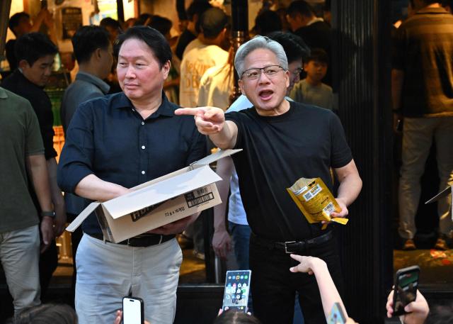 Nvidia CEO Jensen Huang (R) and SK Group Chairman Chey Tae-won (L) hand out "HBM chip" snacks to reporters during their dinner at a Korean barbecue restaurant in Seoul on June 5, 2026. Nvidia chief executive Jensen Huang arrived in Seoul on June 5, for a packed schedule of meetings with tech leaders, promising "some surprises" for South Korea while predicting robotics will be the country's next major growth sector. (Photo by Jung Yeon-je / AFP)