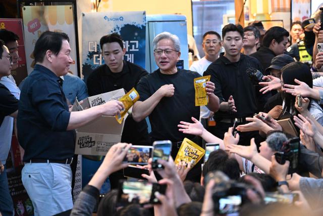 Nvidia CEO Jensen Huang (C) and SK Group Chairman Chey Tae-won (L) hand out "HBM chip" snacks to reporters during their dinner at a Korean barbecue restaurant in Seoul on June 5, 2026. Nvidia chief executive Jensen Huang arrived in Seoul on June 5, for a packed schedule of meetings with tech leaders, promising "some surprises" for South Korea while predicting robotics will be the country's next major growth sector. (Photo by Jung Yeon-je / AFP)