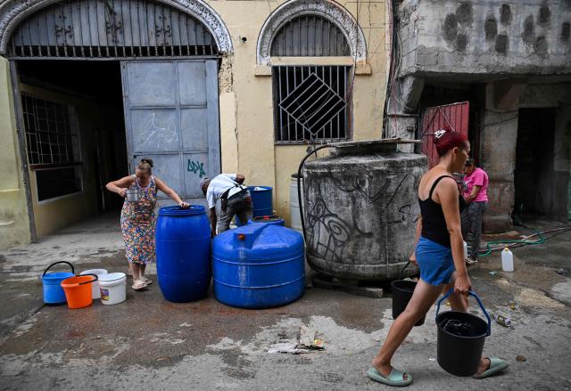 People fill buckets and containers with water from storage tanks on a street in Havana on June 5, 2026. (Photo by YAMIL LAGE / AFP)