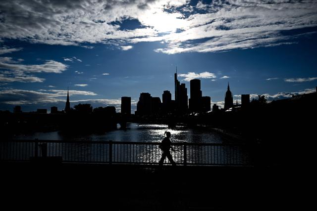 A woman walks on a bridge in front of the banking district skyline with the Commerzbank building (4th R) and the Cathedral (2nd R) during sunset in Frankfurt am Main, western Germany, on June 5, 2026. (Photo by Kirill KUDRYAVTSEV / AFP)