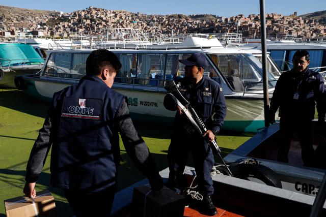 A police officer stands guard as workers from the National Office of Electoral Processes (ONPE) load electoral material onto a boat bound for the islands of Amantani in Lake Titicaca, in Puno, southern Peru, on June 5, 2026. Right-wing candidate Keiko Fujimori and leftist Roberto Sanchez will face off in Peru's presidential runoff on June 7, 2026. (Photo by Juan Carlos CISNEROS / AFP)