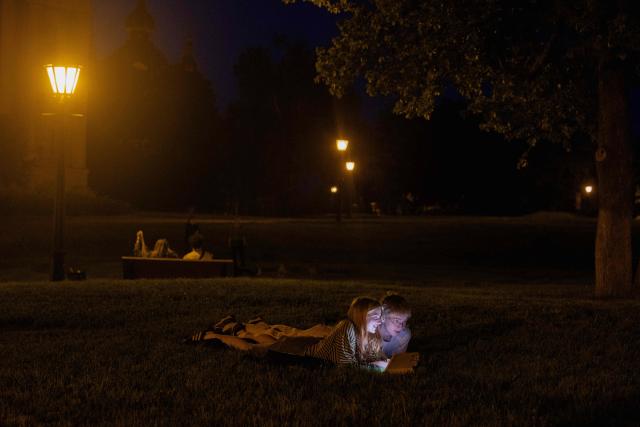 Teenagers lay on the grass in the evening in Kyiv on June 5, 2026, amid the Russian invasion of Ukraine. (Photo by Tetiana DZHAFAROVA / AFP)