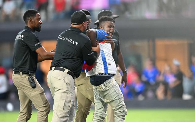 Security agents escors a fan who rushed the pitch during the international friendly football match between Haiti and Peru at Nu Stadium in Miami, Florida on June 5, 2026. (Photo by CHANDAN KHANNA / AFP)