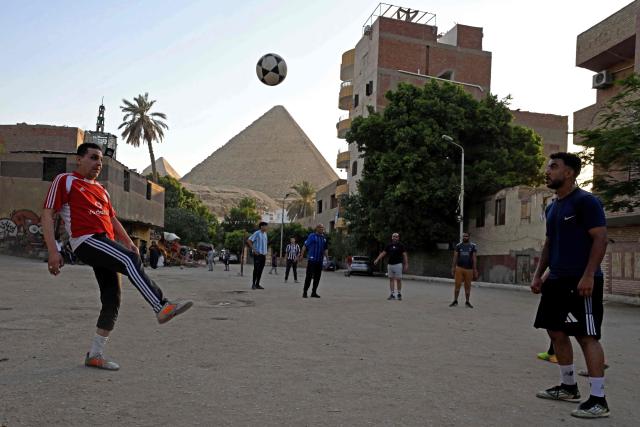 Egyptians play football along a street in Nazlet el-Semman neighbourhood next to the Great Pyramids of Giza in Cairo on June 5, 2026. The Egyptians open their 2026 FIFA World Cup campaign against Belgium in Seattle on June 15 before lining up against New Zealand and Iran in Group G. (Photo by Khaled DESOUKI / AFP)