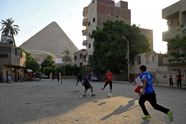 Egyptians play football along a street in Nazlet el-Semman neighbourhood next to the Great Pyramids of Giza in Cairo on June 5, 2026. The Egyptians open their 2026 FIFA World Cup campaign against Belgium in Seattle on June 15 before lining up against New Zealand and Iran in Group G. (Photo by Khaled DESOUKI / AFP)