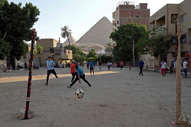 Egyptians play football along a street in Nazlet el-Semman neighbourhood next to the Great Pyramids of Giza in Cairo on June 5, 2026. The Egyptians open their 2026 FIFA World Cup campaign against Belgium in Seattle on June 15 before lining up against New Zealand and Iran in Group G. (Photo by Khaled DESOUKI / AFP)