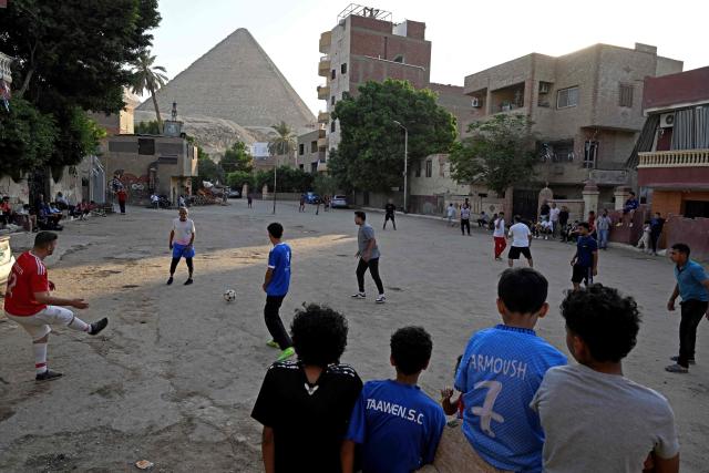 Egyptians play football along a street in Nazlet el-Semman neighbourhood next to the Great Pyramids of Giza in Cairo on June 5, 2026. The Egyptians open their 2026 FIFA World Cup campaign against Belgium in Seattle on June 15 before lining up against New Zealand and Iran in Group G. (Photo by Khaled DESOUKI / AFP)