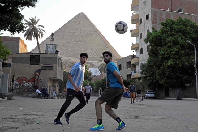 Egyptians play football along a street in Nazlet el-Semman neighbourhood next to the Great Pyramids of Giza in Cairo on June 5, 2026. The Egyptians open their 2026 FIFA World Cup campaign against Belgium in Seattle on June 15 before lining up against New Zealand and Iran in Group G. (Photo by Khaled DESOUKI / AFP)