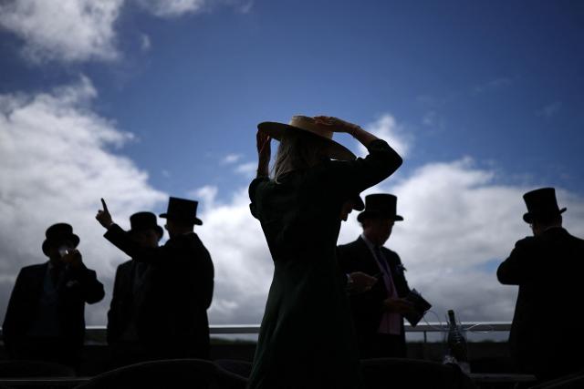 A racegoer holds on to her hat ahead of racing on the second day of the Epsom Derby Festival horse racing event in Surrey, southern England on June 6, 2026. (Photo by Henry NICHOLLS / AFP)