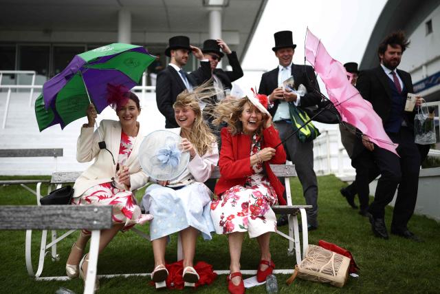 Racegoers fight against the windy conditions ahead of racing on the second day of the Epsom Derby Festival horse racing event in Surrey, southern England on June 6, 2026. (Photo by Henry NICHOLLS / AFP)