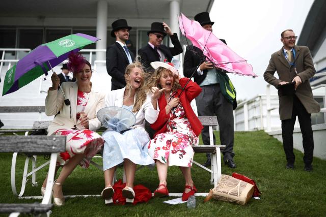 Racegoers fight against the windy conditions ahead of racing on the second day of the Epsom Derby Festival horse racing event in Surrey, southern England on June 6, 2026. (Photo by Henry NICHOLLS / AFP)