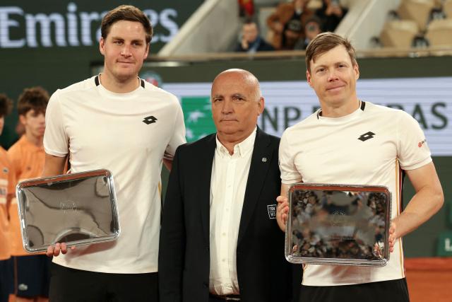 Great Britain's Henry Patten (L) and Finland's Harri Heliovaraa (R), flanked by Philippe Belou, FFT's Vice-President in charge of metropolitan and overseas territories, clubs, and relations with local authorities, pose with their trophies after being defeated by Spain's Marcel Granollers and Argentina's Horacio Zeballos during their men's doubles final match on day 14 of the French Open tennis tournament on Court Philippe-Chatrier at the Roland-Garros Complex in Paris on June 6, 2026. (Photo by Alain JOCARD / AFP)