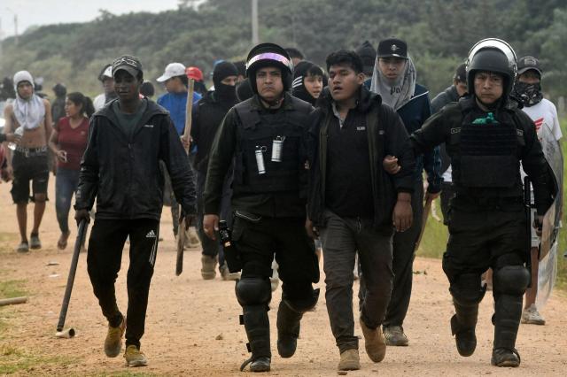 Police officers escort a detained anti-government demonstrator during clashes amid an operation to clear a road blockade in San Julian, Santa Cruz department, Bolivia, on June 6, 2026. Bolivia has faced days of demonstrations and road blockades amid growing political tensions and shortages affecting different regions of the country. (Photo by Rodrigo URZAGASTI / AFP)