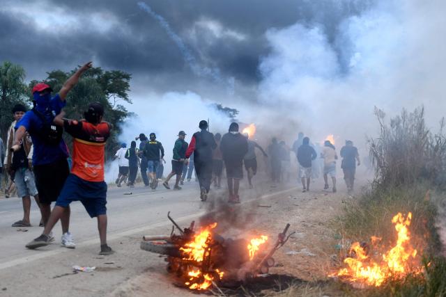 A motorcycle burns near anti-government demonstrators during clashes with police and civilians amid an operation to clear a road blockade in San Julian, Santa Cruz department, Bolivia, on June 6, 2026. Bolivia has faced days of demonstrations and road blockades amid growing political tensions and shortages affecting different regions of the country. (Photo by Rodrigo URZAGASTI / AFP)