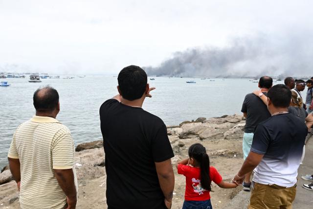 A man points to burning fishing boats near the port of Manta, Ecuador on June 6, 2026. At least 35 fishing boats were destroyed and two people were injured in a major fire that broke out at a crowded dock in western Ecuador on June 6, 2026, according to the Risk Management Secretariat. The Ecuadorian Police stated in a press release that "the incident appears to have occurred while welding work was being carried out on a boat" and ruled out the possibility that it was an attack by criminal groups. (Photo by ARIEL OCHOA / AFP)