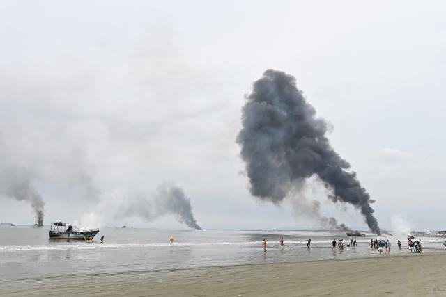 Ecuadorian firefighters and people extinguish a fire on fishing boats near the port of Manta, Ecuador on June 6, 2026. At least 35 fishing boats were destroyed and two people were injured in a major fire that broke out at a crowded dock in western Ecuador on June 6, 2026, according to the Risk Management Secretariat. The Ecuadorian Police stated in a press release that "the incident appears to have occurred while welding work was being carried out on a boat" and ruled out the possibility that it was an attack by criminal groups. (Photo by ARIEL OCHOA / AFP)