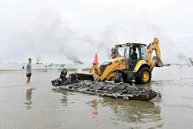 A backhoe removes clears the wreckage of a burned-out fishing boat near the port of Manta, Ecuador on June 6, 2026. At least 35 fishing boats were destroyed and two people were injured in a major fire that broke out at a crowded dock in western Ecuador on June 6, 2026, according to the Risk Management Secretariat. The Ecuadorian Police stated in a press release that "the incident appears to have occurred while welding work was being carried out on a boat" and ruled out the possibility that it was an attack by criminal groups. (Photo by Ariel OCHOA / AFP)