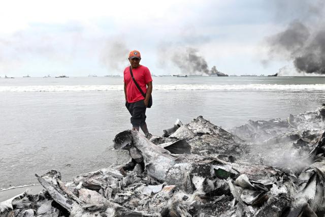 A man looks at the wreckage of a burned-out fishing boat near the port of Manta, Ecuador on June 6, 2026. At least 35 fishing boats were destroyed and two people were injured in a major fire that broke out at a crowded dock in western Ecuador on June 6, 2026, according to the Risk Management Secretariat. The Ecuadorian Police stated in a press release that "the incident appears to have occurred while welding work was being carried out on a boat" and ruled out the possibility that it was an attack by criminal groups. (Photo by ARIEL OCHOA / AFP)