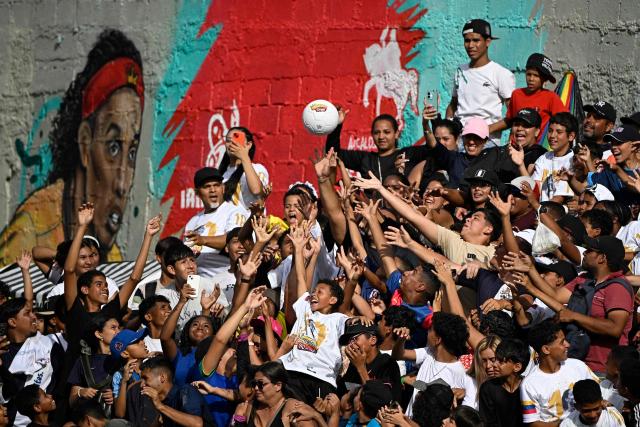 Football fans reach for a ball as they enjoy the Monumental League exhibition football match between CLX Futbol and Patacones FC featuring Brazil former football star Ronaldinho at the Mesuca community in the Petare neighborhood in Caracas on June 6, 2026. (Photo by Federico PARRA / AFP)