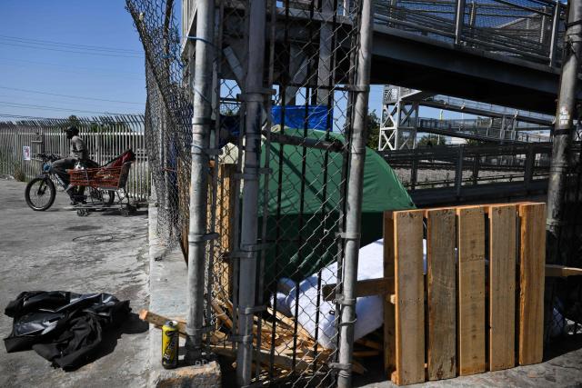 A person on a bicycle pulls a shopping cart near a homeless encampment in the Panorama City neighborhood of Los Angeles, California on June 1, 2026. Los Angeles, the second-largest US city prepares to host eight World Cup soccer matches this summer, followed by the 2028 Olympics. Infamous for its squalid encampments—located right on the sidewalks or beneath massive highway overpasses—the "City of Angels" has been pulling out all the stops over the past three years to house its homeless population. Democratic Mayor Karen Bass has made this a top priority, ramping up initiatives to fund thousands of housing spots, whether in hotels or in "tiny homes" (Photo by Patrick T. Fallon / AFP)