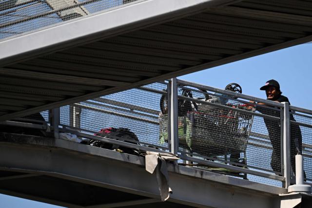 A person pushes a shopping cart over a pedestrian train overpass near a homeless encampment in the Panorama City neighborhood of Los Angeles, California on June 1, 2026. Los Angeles, the second-largest US city prepares to host eight World Cup soccer matches this summer, followed by the 2028 Olympics. Infamous for its squalid encampments—located right on the sidewalks or beneath massive highway overpasses—the "City of Angels" has been pulling out all the stops over the past three years to house its homeless population. Democratic Mayor Karen Bass has made this a top priority, ramping up initiatives to fund thousands of housing spots, whether in hotels or in "tiny homes" (Photo by Patrick T. Fallon / AFP)