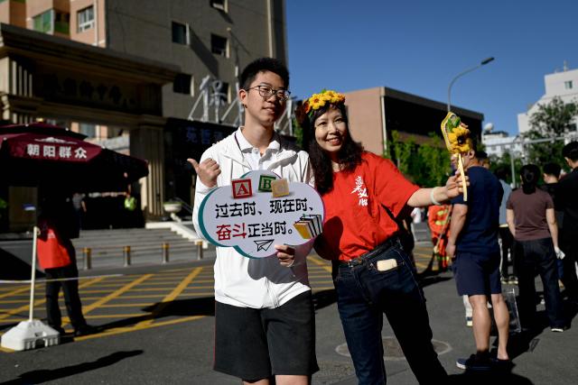 A student (L) holding a poster reading "The past, The present, Now is the time to strive" poses for a picure with his teacher before entering a school on the first day of China's National College Entrance Examination (NCEE) known as "gaokao", in Beijing on June 7, 2026. (Photo by WANG Zhao / AFP)