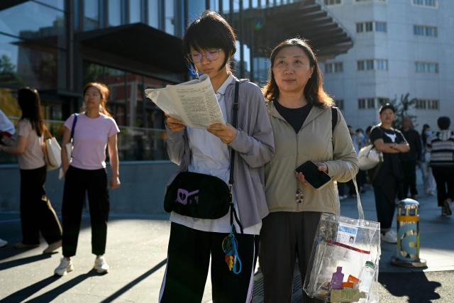 A student reads a book before entering a school on the first day of China's National College Entrance Examination (NCEE) known as "gaokao", in Beijing on June 7, 2026. (Photo by WANG Zhao / AFP)