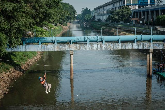 A woman shouts as she glides across the Ciliwung River on a zip line in Jakarta on June 7, 2026. (Photo by Yasuyoshi Chiba / AFP)