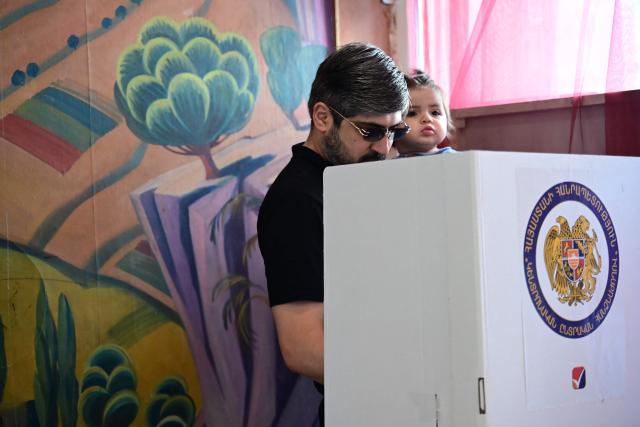 A man holding a child votes in Armenia's parliamentary election at a polling station in Yerevan on June 7, 2026. (Photo by Karen MINASYAN / AFP)